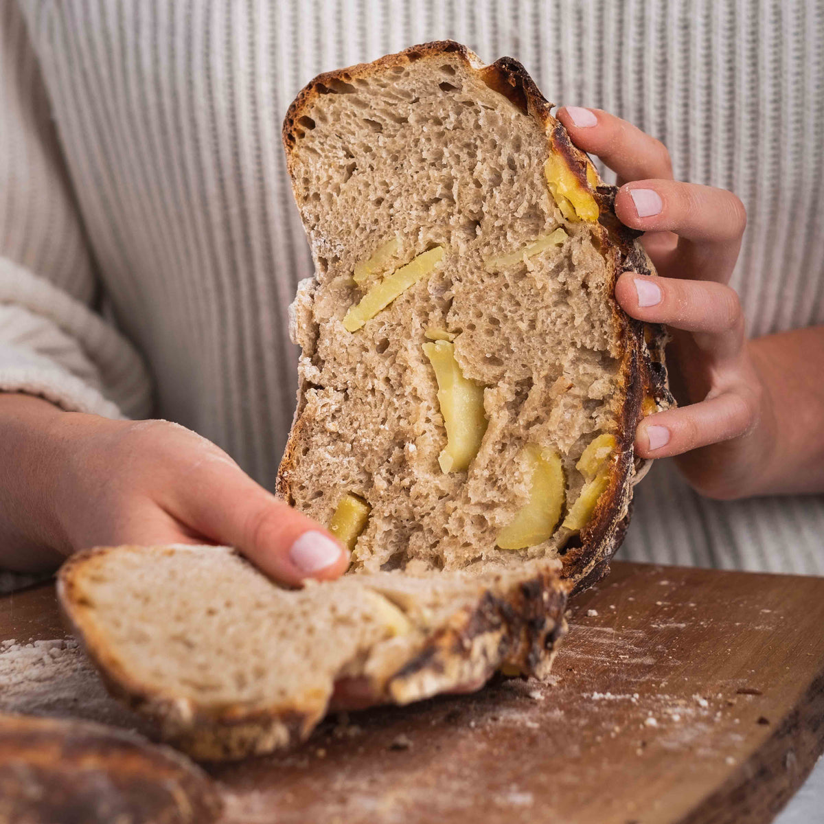 Zwei Hände halten ein aufgeschnittenes Kartoffelbrot über einem Holzbrett 